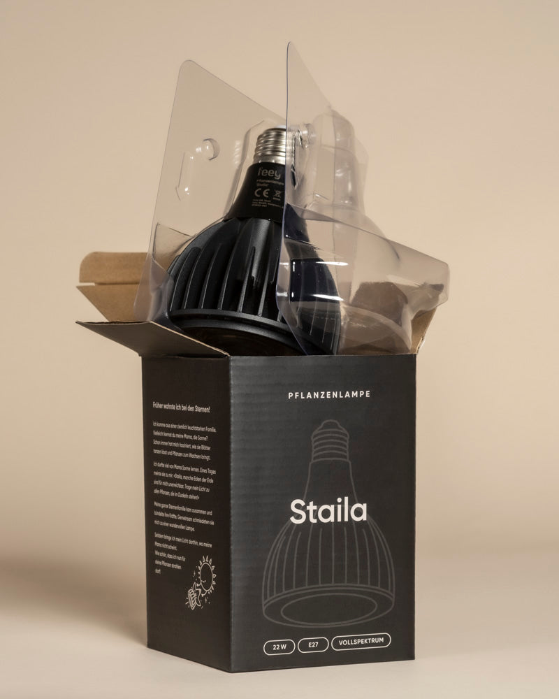 Eine schwarze Pflanzenlampe, die teilweise aus der geöffneten Schachtel genommen wurde, ist in durchsichtiges Plastik gehüllt. Die Verpackung trägt den Namen 