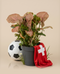 Eine getopfte Syngonium 'Neon' - feey mit leuchtend rosa-grünen Blättern sitzt in einem einfachen schwarzen Topf vor einem schlichten beigen Hintergrund.